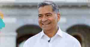Smiling middle-aged man with gray hair in a white shirt, outdoors, with a turquoise logo partially visible on the left.