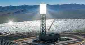 Wide view of a solar power plant with a central tower surrounded by rows of solar mirrors in a desert valley.”] ,
