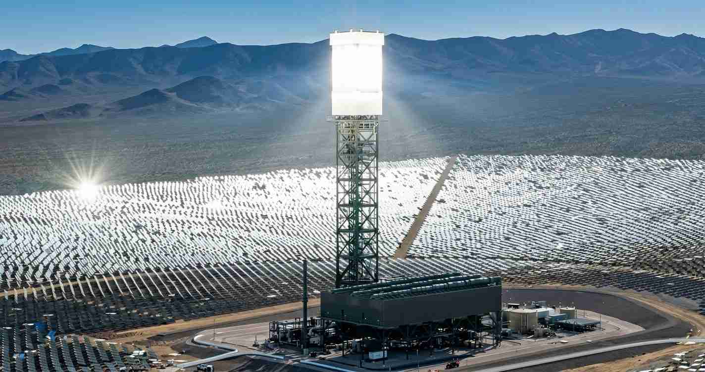 Wide view of a solar power plant with a central tower surrounded by rows of solar mirrors in a desert valley.”] ,