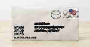 White envelope on a light wood surface featuring a QR code and the caption 'SCAN TO LEARN MORE,' plus a US stamp and postmark.