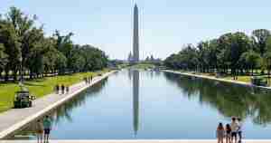 Reflecting pool with the Washington Monument in the distance, trees along both sides, and people walking along the paths.