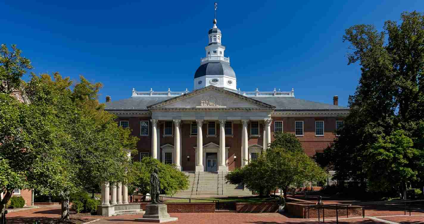 Brick university building with white columns and a blue dome, set in a courtyard with trees and statue in front.