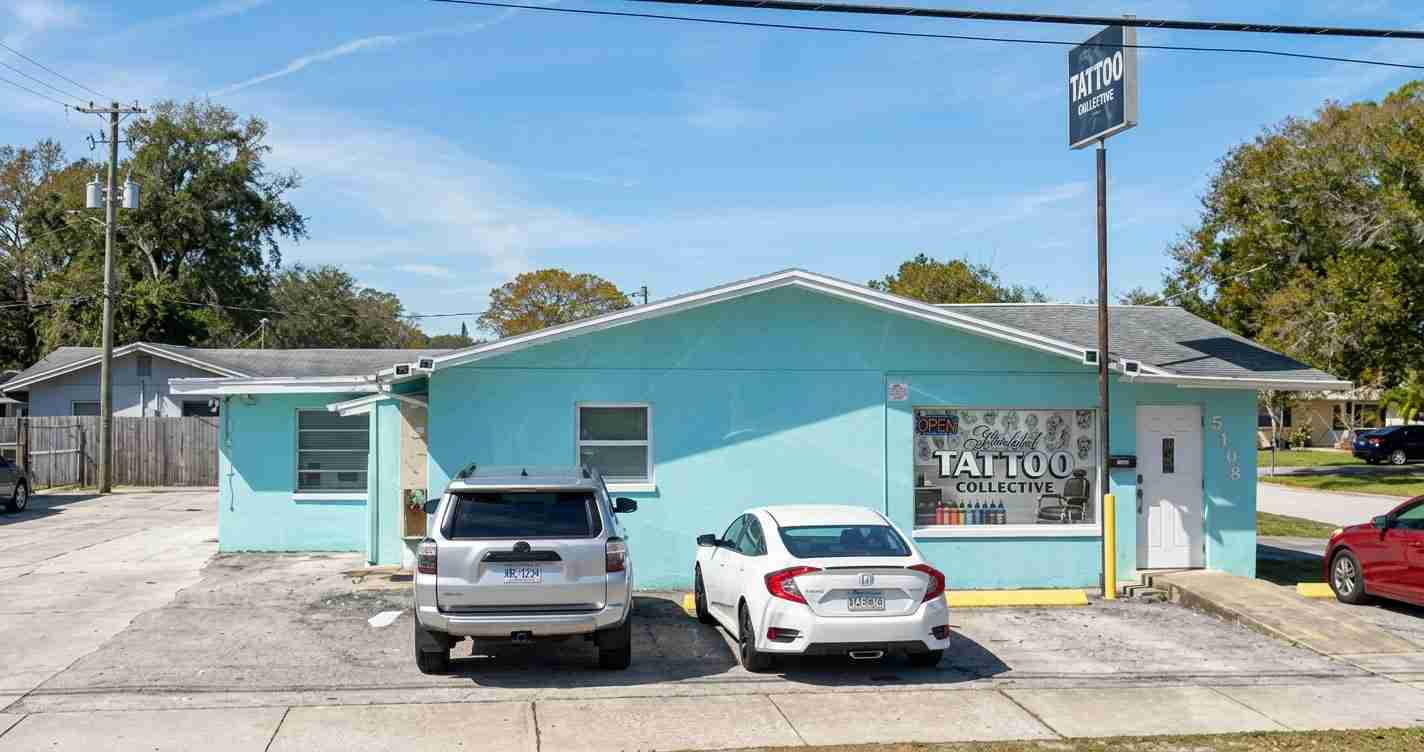 Turquoise single-story tattoo shop with a large window sign reading 'Tattoo Collective' and two parked cars in front of the building.