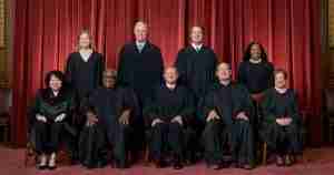 Group portrait of nine people in black judicial robes posing for a formal photo in front of red stage curtains.