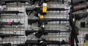 Assorted rifles and shotguns displayed on a metal grid wall in a gun shop with price tags visible.