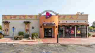 Taco Bell restaurant exterior with orange entrance and purple bell logo under a pale blue sky